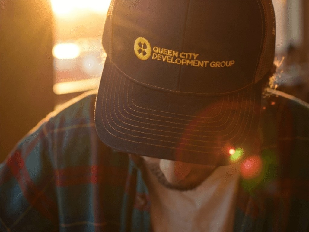 A person wearing a cap with "Queen City Development Group" branding, captured in warm sunlight.
